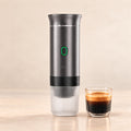 Metallic grey portable espresso maker with a glass of fresh espresso